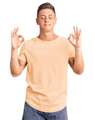 Young handsome man wearing casual clothes relaxed and smiling with eyes closed doing meditation gesture with fingers. yoga concept.