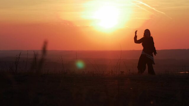 The silhouette of a girl dancing against the background of the sun