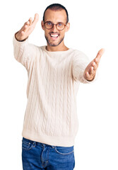 Naklejka premium Young handsome man wearing casual clothes and glasses looking at the camera smiling with open arms for hug. cheerful expression embracing happiness.
