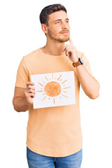 Handsome young man with bear holding sun draw serious face thinking about question with hand on...