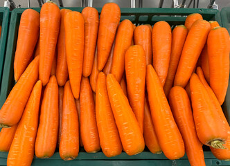 Carrots are on four green boxes in a supermarket.