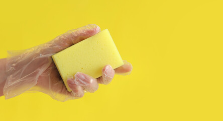 A yellow sponge for washing dishes in a woman’s hand on a yellow background. A hand in a transparent disposable glove holds a sponge for wet cleaning. Professional cleaning. Copy space