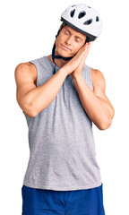 Young handsome man wearing bike helmet sleeping tired dreaming and posing with hands together while smiling with closed eyes.