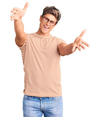 Young handsome man wearing casual clothes and glasses looking at the camera smiling with open arms for hug. cheerful expression embracing happiness. - obrazy, fototapety, plakaty