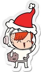 hand drawn sticker cartoon of a happy spacegirl holding moon rock wearing santa hat