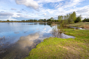 young green grass on the shore of a pond. Bright spring landscape with sky, lake and young trees