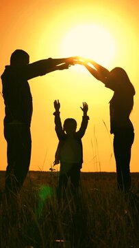 Happy family shows house with their hands, symbol of safety, comfort for child, sunset. Happy family mother father daughter, son, kid, dream to build house, mortgage for family. Silhouette of teamwork