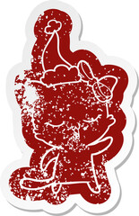 quirky cartoon distressed sticker of a cat with bow on head wearing santa hat