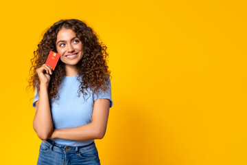 Thoughtful woman with credit card looking at free space on yellow