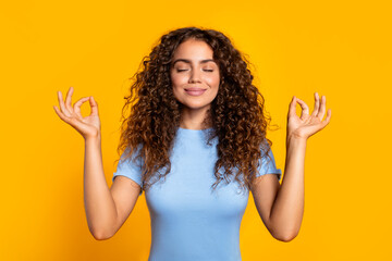 Relaxed woman meditating with hand gestures on yellow