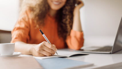 Focused woman writing notes beside laptop, closeup