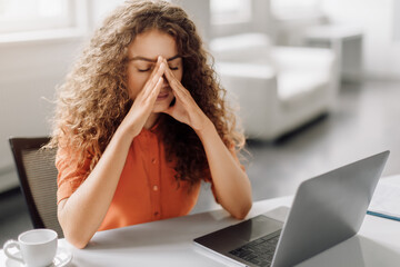 Stressed woman with eyes closed touching nose in front of laptop