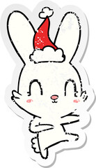 cute hand drawn distressed sticker cartoon of a rabbit dancing wearing santa hat
