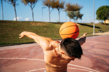 Muscular young shirtless Caucasian guy seen from close up while playing and juggling a basketball on a basketball court.