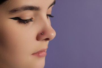 Closeup of a young woman's visage with piercing hanging from her nose.