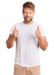 Young caucasian man wearing casual white tshirt success sign doing positive gesture with hand, thumbs up smiling and happy. cheerful expression and winner gesture.