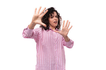 young cute curly-haired caucasian woman dressed in a striped pink blouse actively gesticulates with...