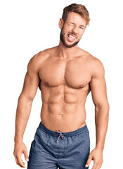 Fototapeta premium Young caucasian man standing shirtless winking looking at the camera with sexy expression, cheerful and happy face.