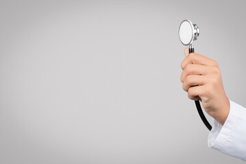 Female doctor holding stethoscope, listening breathing over grey studio background, closeup, free space