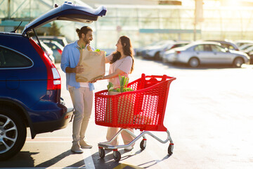 Arab couple by car with grocery bag and cart