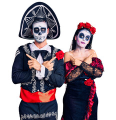 Young couple wearing mexican day of the dead costume over background pointing to both sides with...