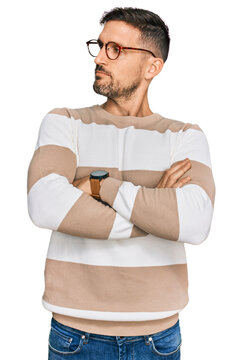 Handsome man with beard wearing casual clothes and glasses looking to the side with arms crossed convinced and confident