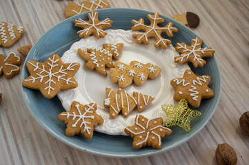 Painted traditional Christmas gingerbreads arranged on blue and white plates on light wooden table, various xmas shapes