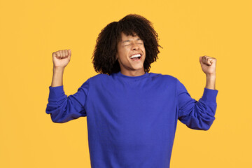 Emotional young black guy celebrating success on yellow studio background