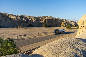 Large tanker truck driving through empty desert canyon in the Mojave desert in Southern California.