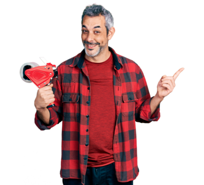 Middle age hispanic with grey hair holding packing tape smiling happy pointing with hand and finger to the side