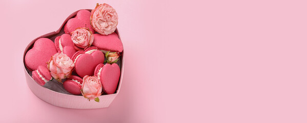Gift box with sweet heart-shaped macarons and beautiful roses on pink background with space for text