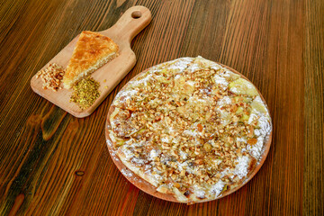 Kunafa with nuts pie walnut, almond and pistachio served in wooden board isolated on table side view of arabic food