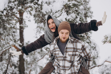 A young happy and loving couple is having fun in a snowy forest in winter.