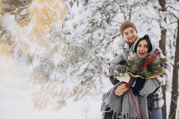 Cute young couple in love with pine bouquet spending time on Valentine's day in snowy winter forest in mountains