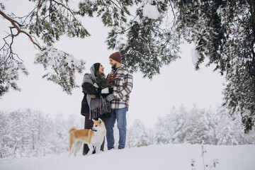Fototapeta na wymiar Happy young couple with akita dog in forest on winter day