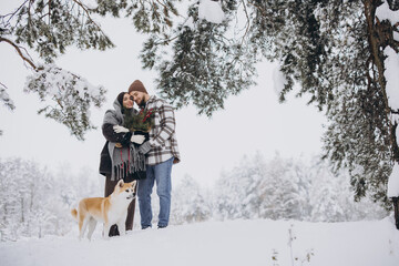 Happy young couple with akita dog in forest on winter day
