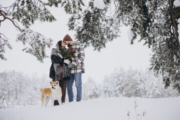 Happy young couple with akita dog in forest on winter day