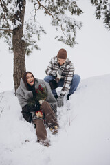 Cute young couple in love with pine bouquet spending time on Valentine's day in snowy winter forest...