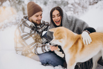 Happy young couple with akita dog in forest on winter day