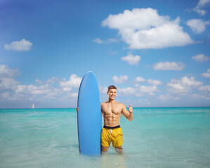 Muscular man with a surfboard standing into the ocean