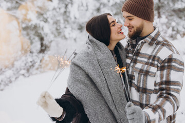Happy romantic couple in love holding sparklers in snowy winter forest