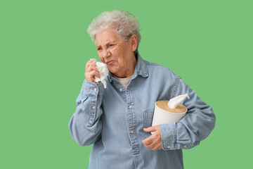 Ill senior woman with tissue box on green background