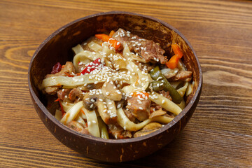 Wok udon noodles with beef and vegetables in a coconut shell plate