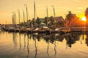 Fototapeta na wymiar Old ships in the port of a city in the Netherlands during sunset. Brown wooden yachts in the calm in the summer