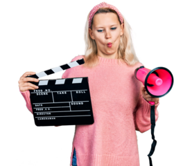 Young caucasian woman holding video film clapboard and megaphone making fish face with mouth and squinting eyes, crazy and comical.