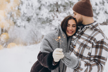 Happy romantic couple in love holding sparklers in snowy winter forest