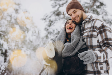 Fototapeta premium Happy romantic couple in love holding sparklers in snowy winter forest