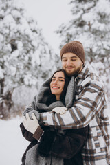 Fototapeta premium A young happy and loving couple is having fun in a snowy forest in winter.