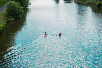 Kayaks Rowing on the River Stream Along a Park in Urban Area