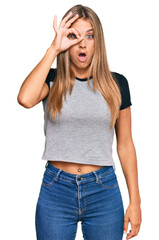 Young blonde woman wearing casual clothes doing ok gesture shocked with surprised face, eye looking through fingers. unbelieving expression.